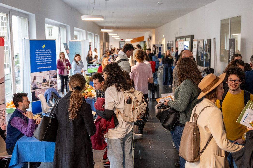 Career Fair all'unibz: un gran numero di persone nel corridoio dell'università e presso gli stand delle aziende.