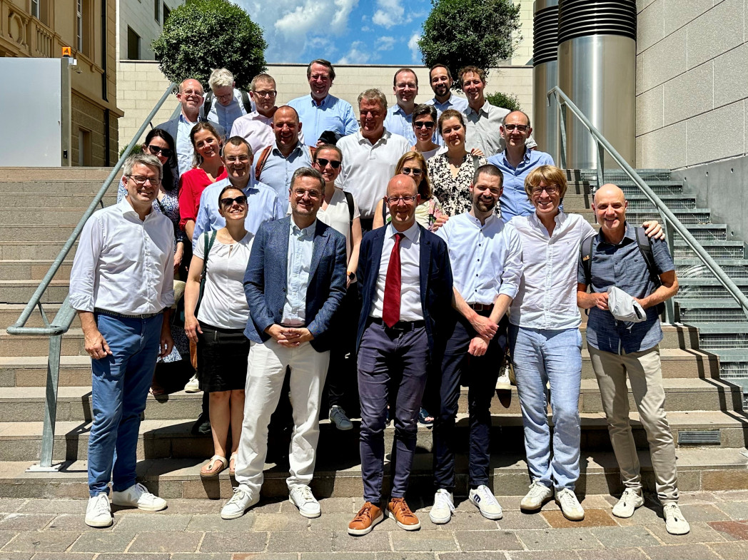 Personen stehen versetzt auf einer Treppe im Außebereich. Es ist ein Gruppenbild.