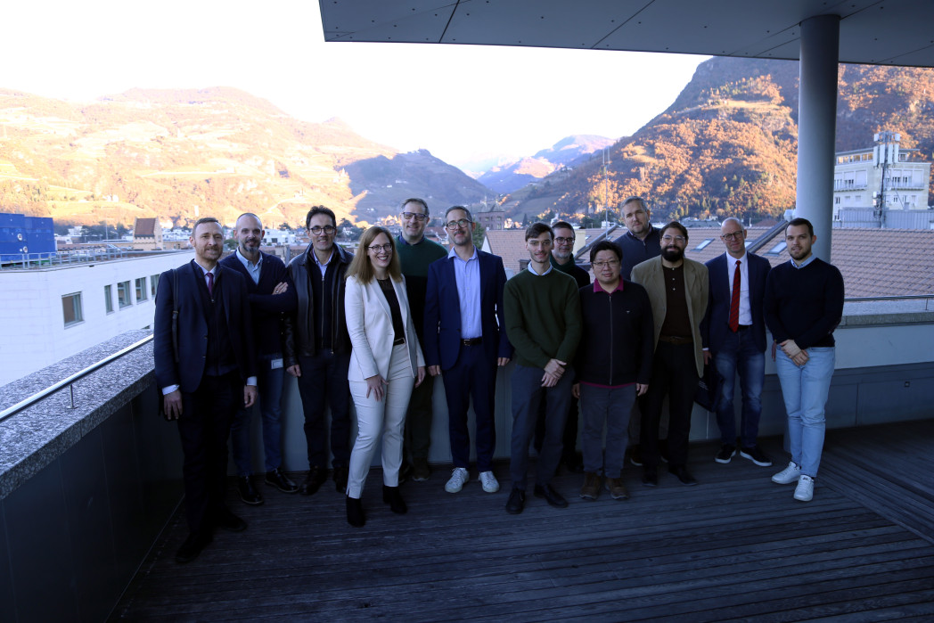 Gruppenbild: 13 Personen astehen auf einer Terrasse - im Hintergrund Dächer der Stadt und Berge.