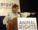 Gary L. Francione sprechend und mit einer erhobenen Hand bei einem Vortrag. Vor und hinter ihm Transparente mit Aufschrift "Animal Rights"