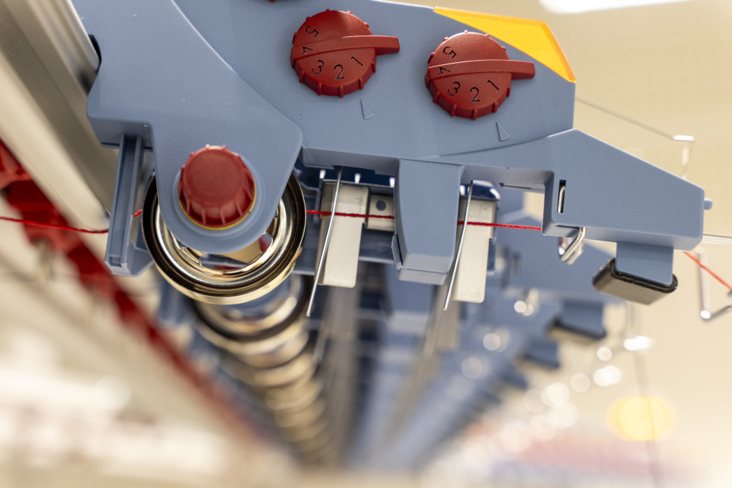 Eine Industriestrickmaschine in Nahaufnahme von der Seite mit einem eingefädelten Faden.