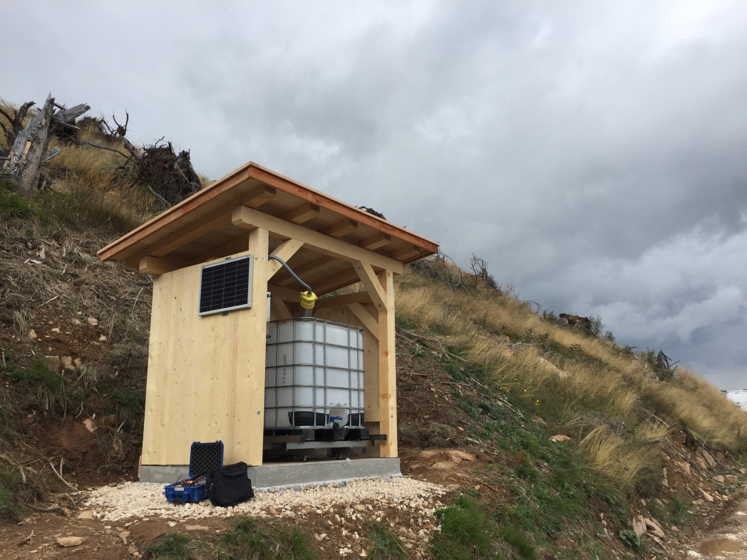 Messtation aus Holz mit Zistern, im Hintergrund Berghang und und bewölkter Himmel