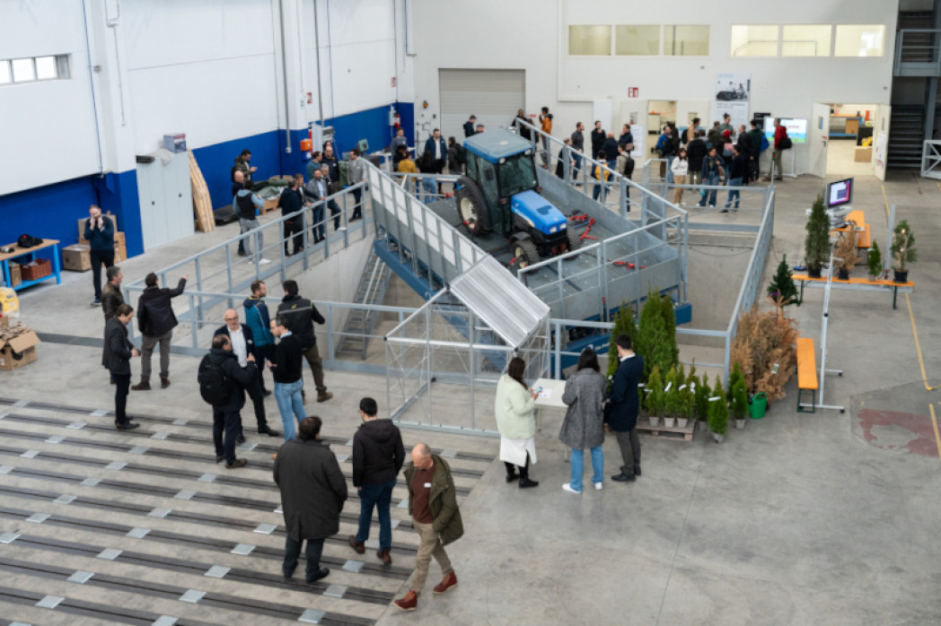 Viele Personen stehen in einer Halle. In der Mitte der Halle befindet sich ein Traktor auf einer technischen Maschine.