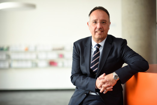 Foto von Prof. Dominik Matt vor dem Hintergrund eines Gangs an unibz, an oranges Teil gelehnt.