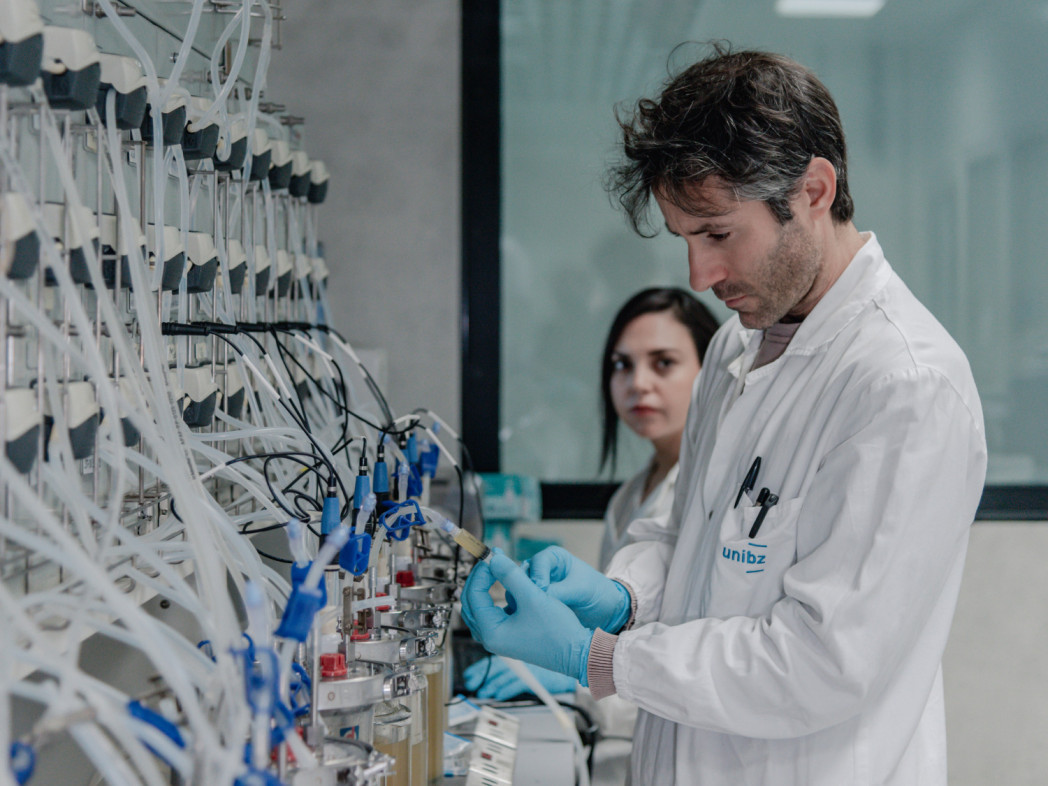 Zwei Personen in einem Lebensmittellabor, in dem viele Schläuche und mit Flüssigkeiten gefüllte Fläschchen  zu sehen sind.