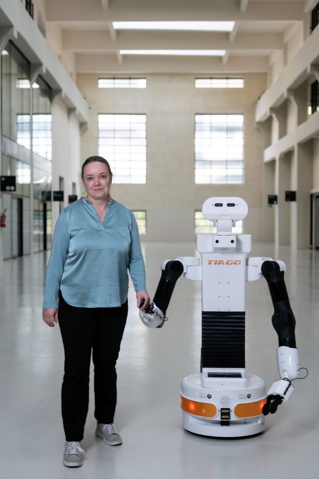 Professorin Peer Hand in Hand mit Roboterplattform Tiago auf einem Gang vor ihrem Labor im NOI Techpark