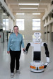 Angelika Peer steht Hand in Hand mit Roboter Tiago in Kranhalle von NOI Techpark